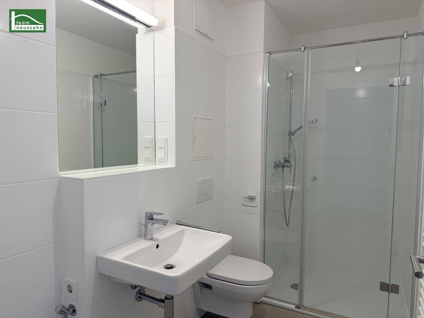 Modernes Badezimmer mit weiß gefliesten Wänden, Duschkabine und wandhängendem WC.
