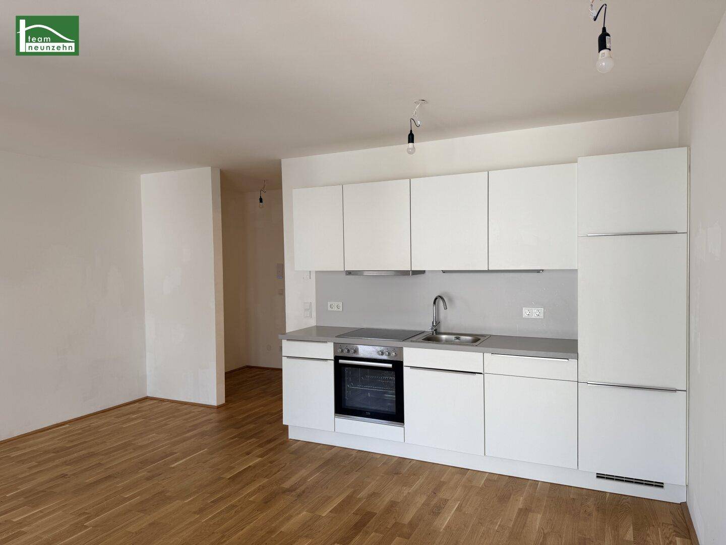 Moderne Einbauküche in Weiß mit Holzparkettboden in einem hellen, offenen Wohnbereich.