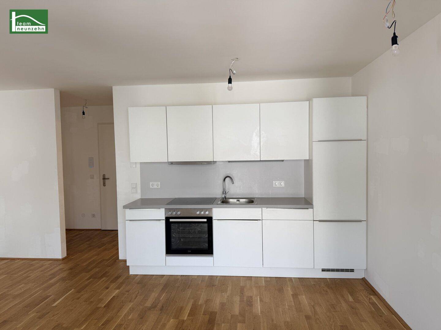 Funktionale weiße Einbauküche mit Backofen und Holzparkett in einem lichtdurchfluteten Raum.