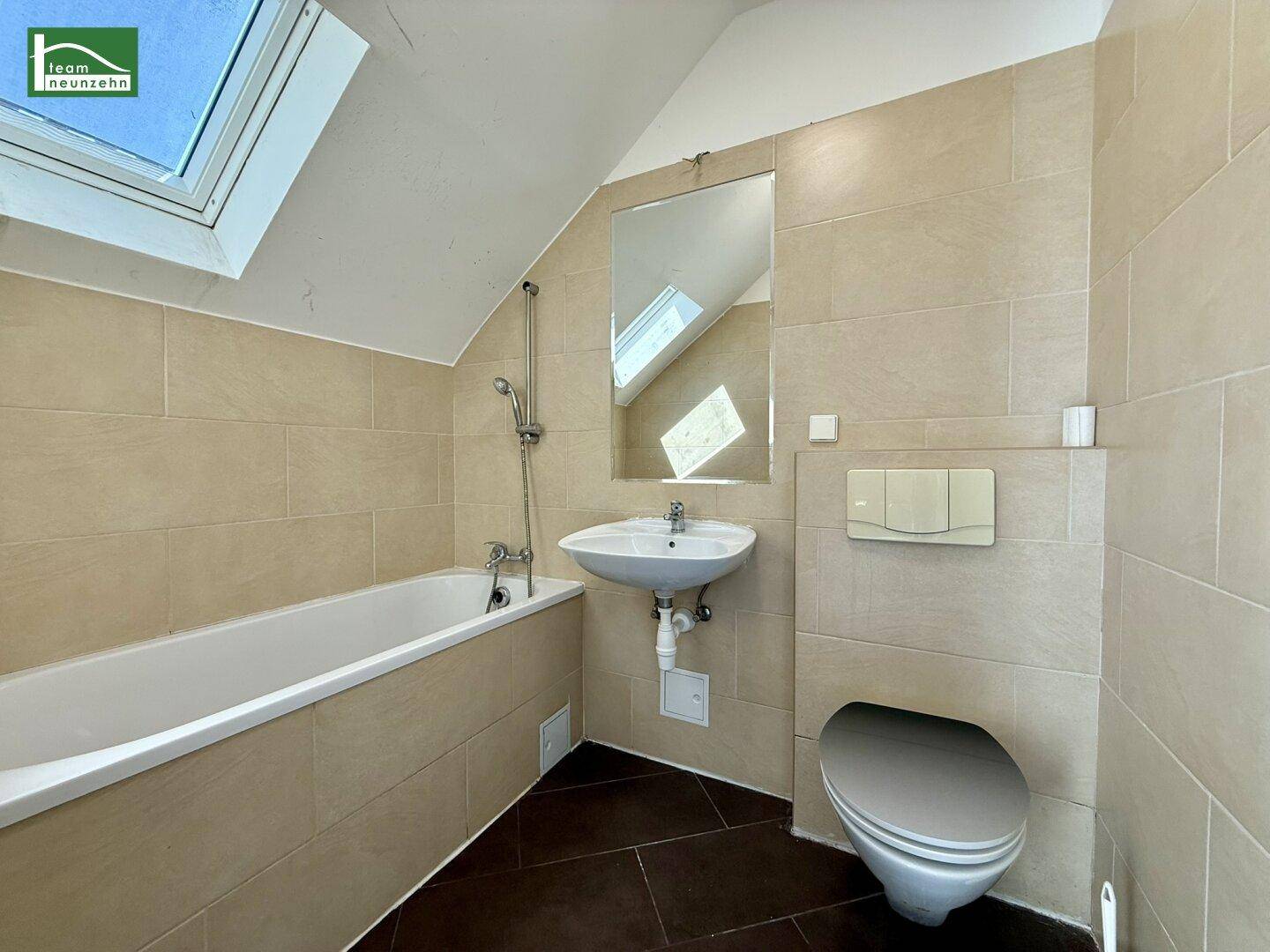 Helles Badezimmer mit Badewanne, WC, Waschbecken, beigen Fliesen und Dachfenster.