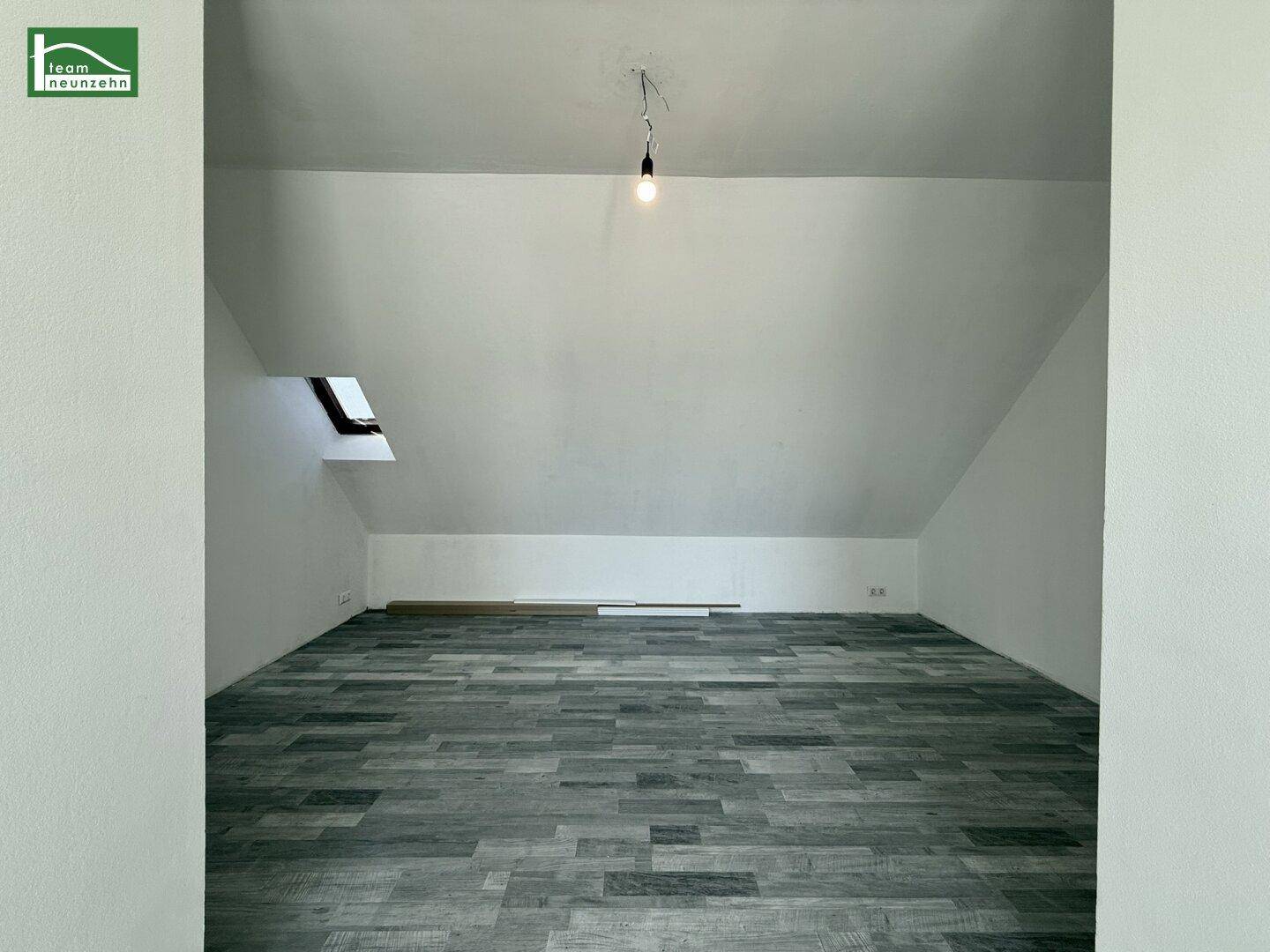 Leerer Raum im Dachgeschoss mit modernem grauen Bodenbelag, Schrägen und einem Dachfenster.
