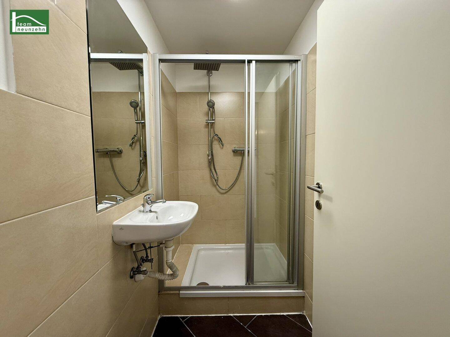 Modernes Badezimmer mit Duschkabine, Waschbecken, Spiegel und beigefarbenen Wandfliesen.