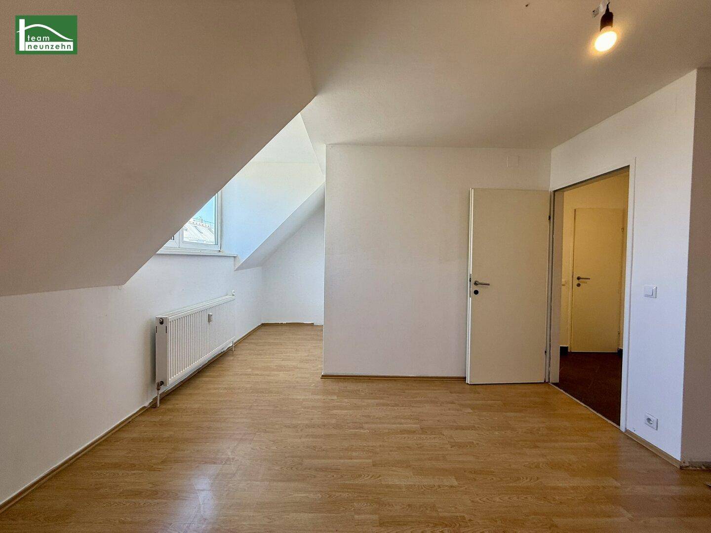 Geräumiger, heller Raum im Dachgeschoss mit Holzfußboden, Schrägen und Heizkörper.