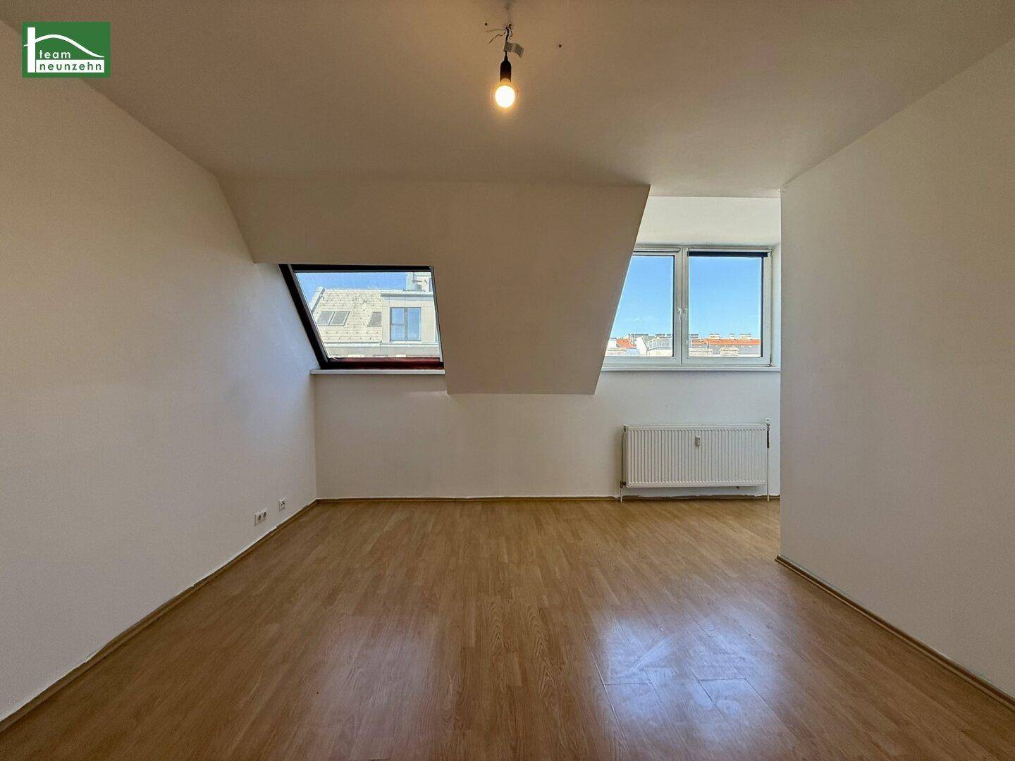 Lichtdurchfluteter Raum im Dachgeschoss mit Holzfußboden, Schrägen und verschiedenen Fenstern.