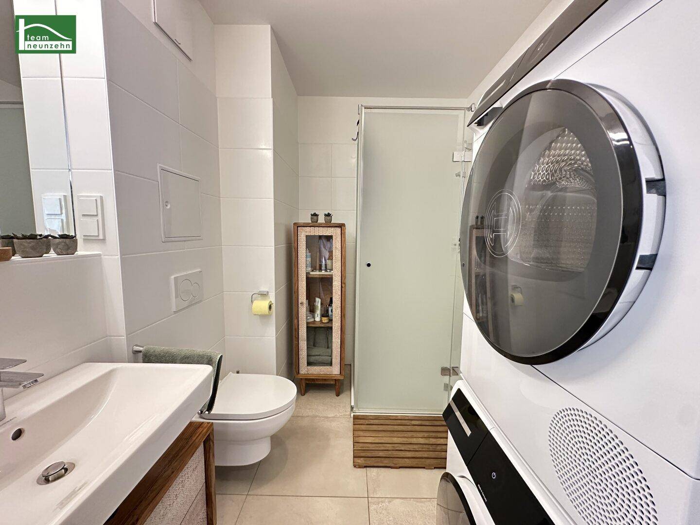 Modernes Badezimmer mit Dusche, Waschbecken und integrierter Waschmaschine und Trockner.
