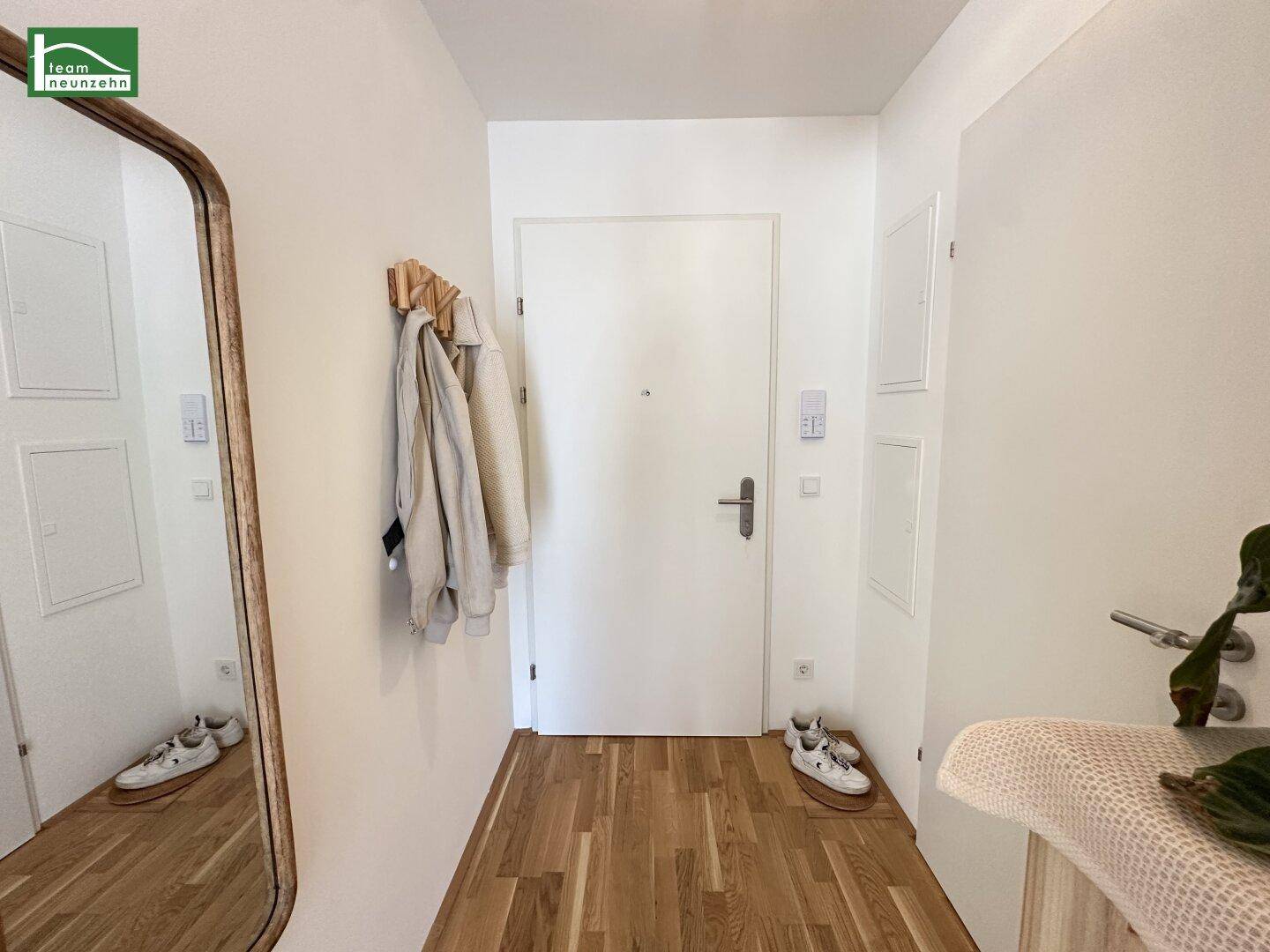 Eingangsbereich mit Holzboden, Garderobe und großem Spiegel, der den Raum erweitert.