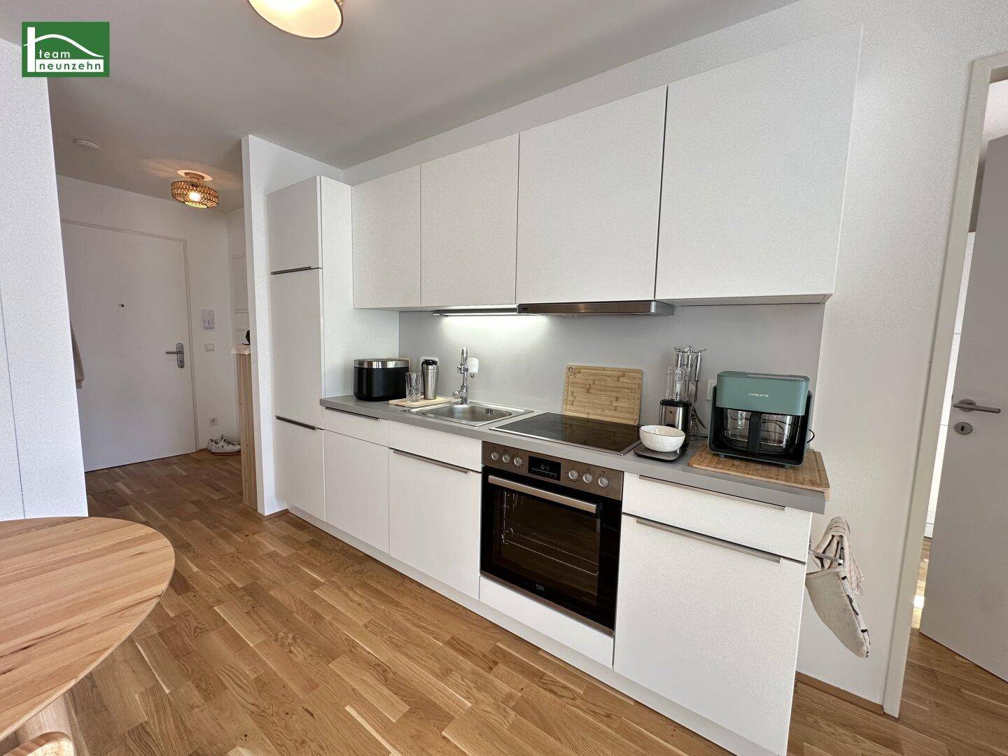 Moderne Einbauküche mit weißen Fronten, Induktionskochfeld und Holzboden.