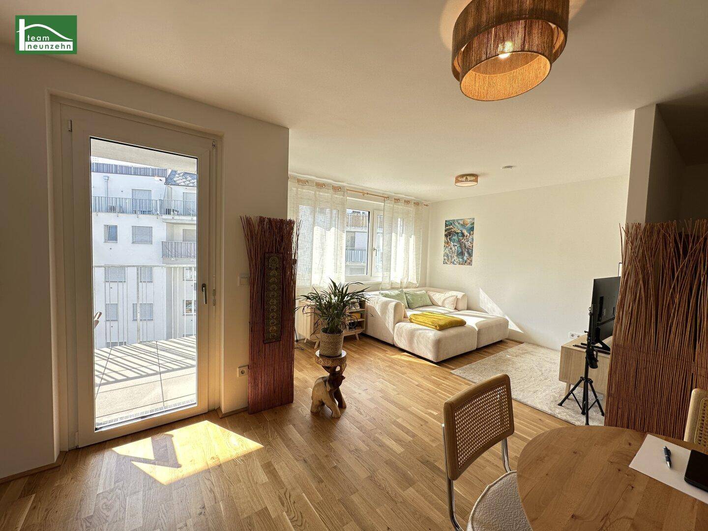 Helles Wohnzimmer mit Balkonzugang, Holzboden und Blick auf die umliegenden Gebäude.