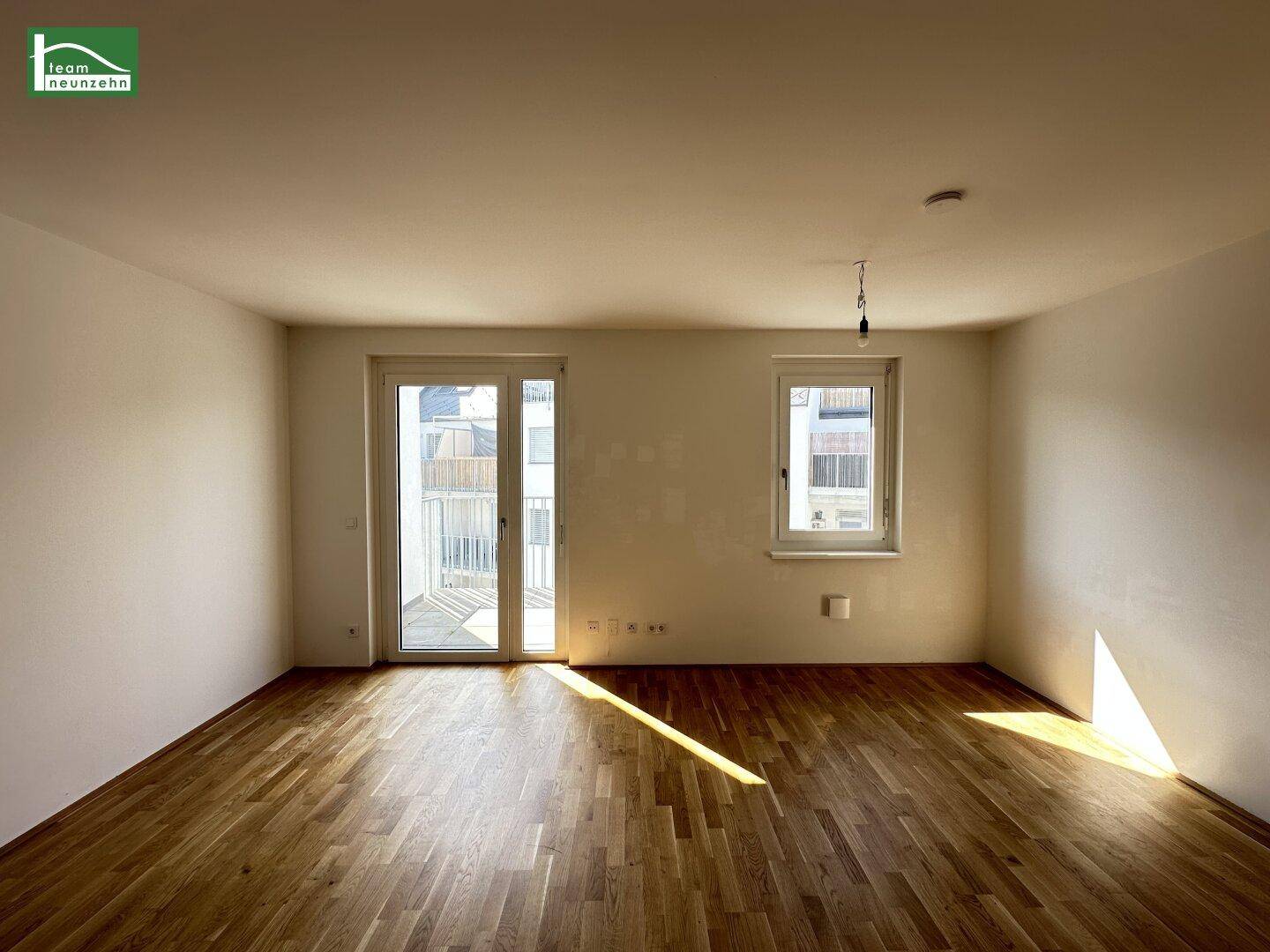Lichtdurchflutetes Wohnzimmer mit Holzboden, Balkontür und großem Fenster.