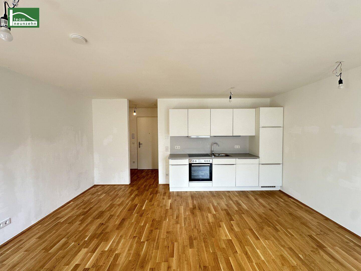 Offener Wohnbereich mit Holzboden und integrierter, moderner Küchenzeile.