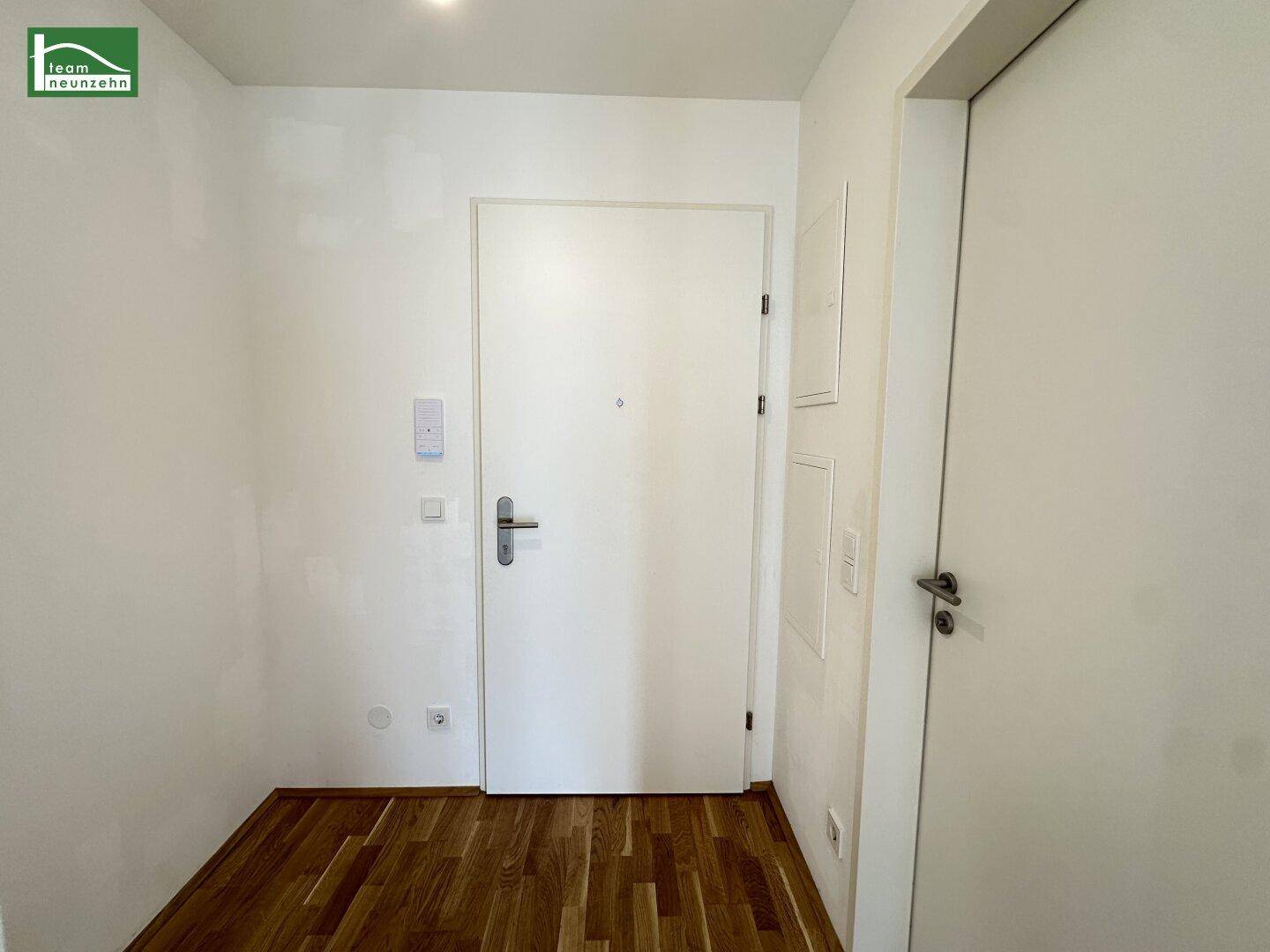 Heller Eingangsbereich mit Holzboden und weißer Wohnungstür.