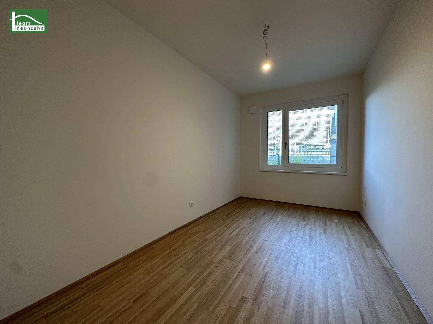 Leeres Zimmer mit Parkettboden und großem Fenster, bietet viel Tageslicht und flexible Gestaltungsmöglichkeiten.