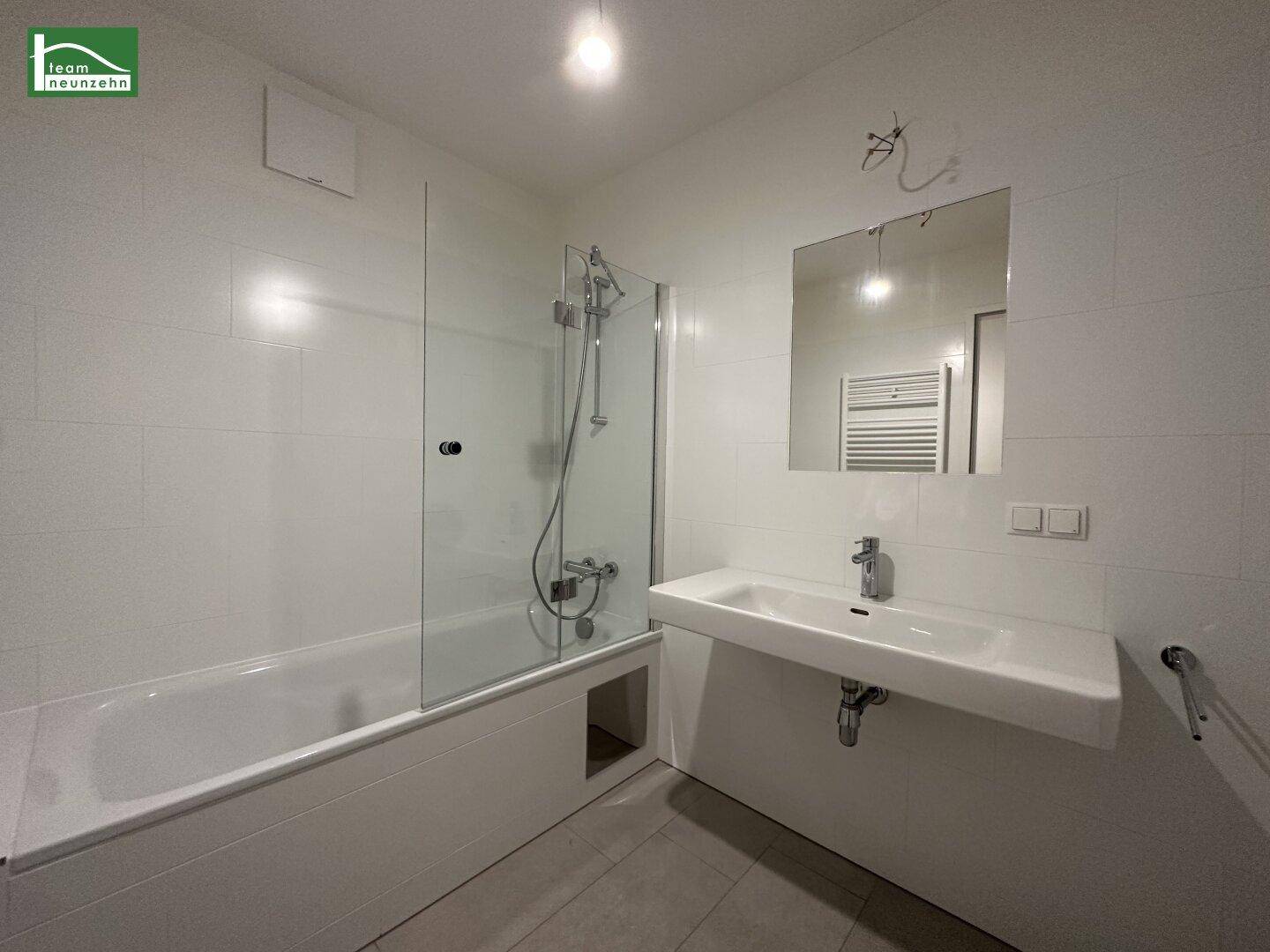 Modernes Badezimmer mit Badewanne, Duschwand, Einzelwaschbecken und beheiztem Handtuchhalter.