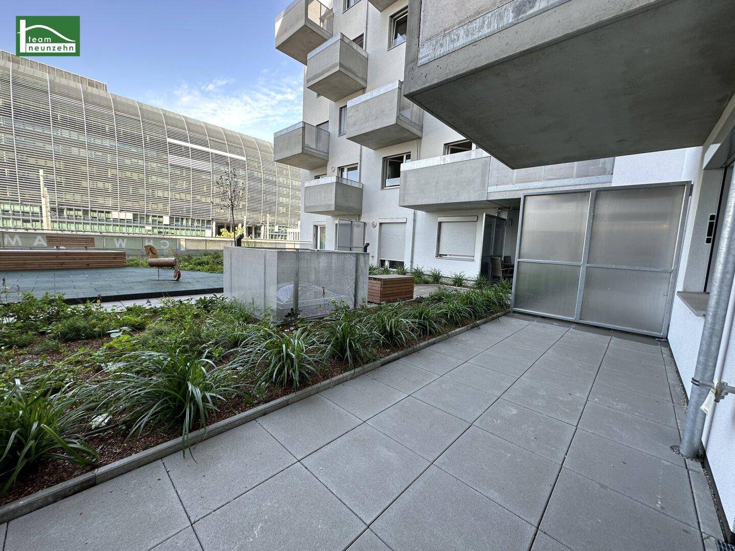 Gepflasterte Terrasse mit Grünflächen und Blick auf die moderne Wohnanlage, ideal für Entspannung.