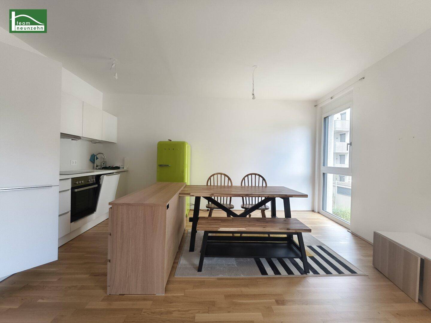 Moderne Küche mit weißen Schränken, Holzboden und Essbereich mit Holztisch.
