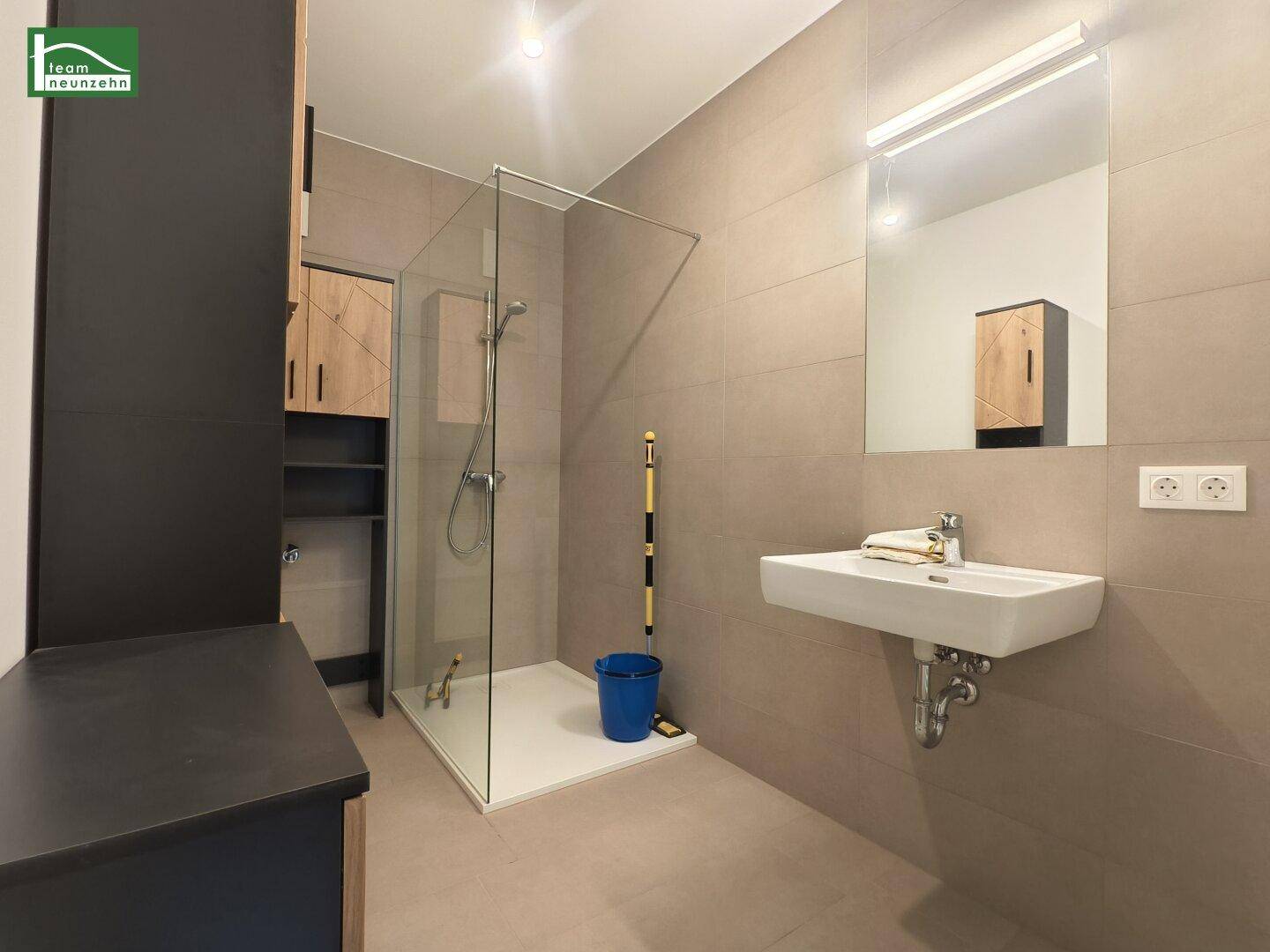 Modernes Badezimmer mit begehbarer Dusche, Wandwaschbecken und großen Fliesen.