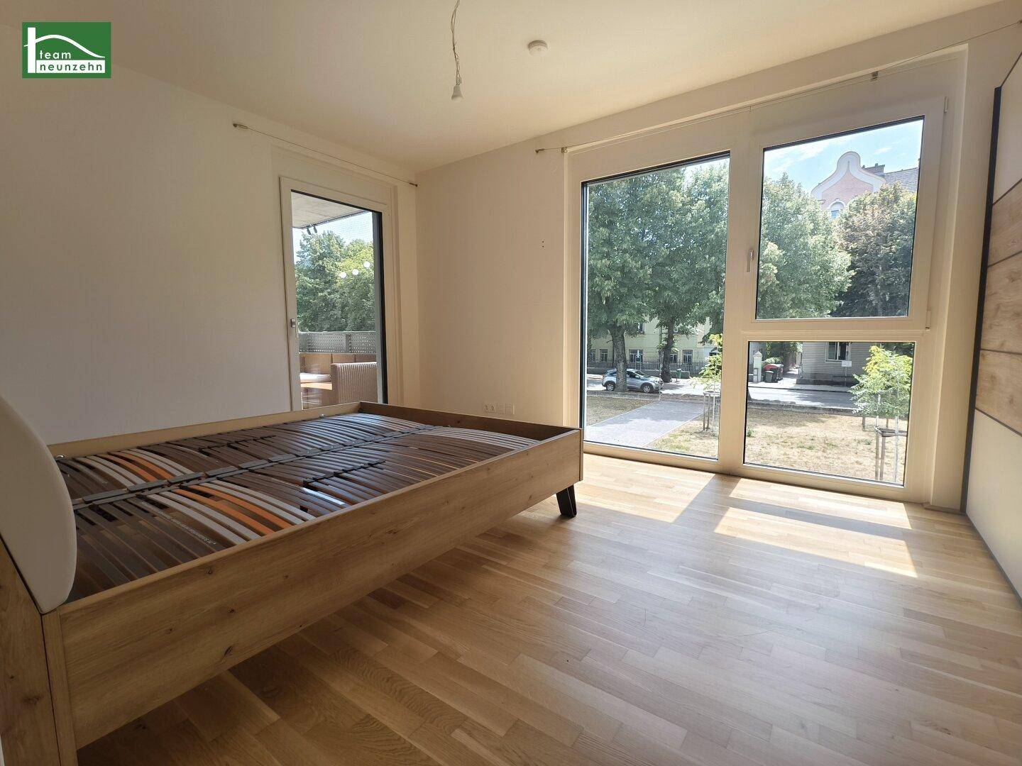 Helles Schlafzimmer mit Holzboden, großen Fenstern und Zugang zu einem Balkon.