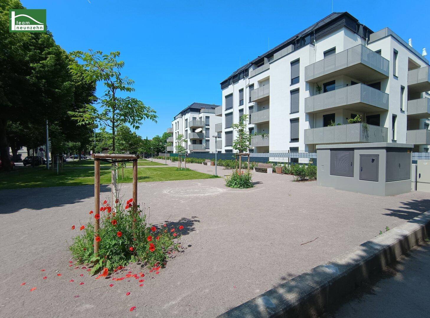 Moderne Wohngebäude mit gepflegten Grünflächen und Bäumen unter blauem Himmel.
