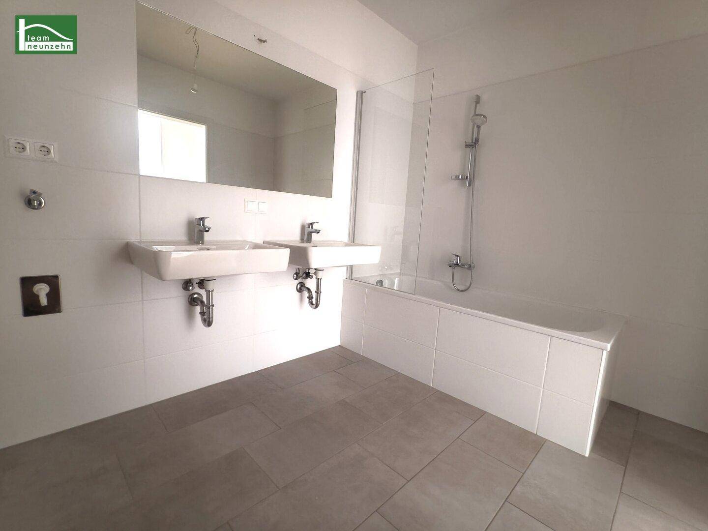 Modernes Badezimmer mit Doppelwaschbecken, Badewanne und großen weißen Fliesen.