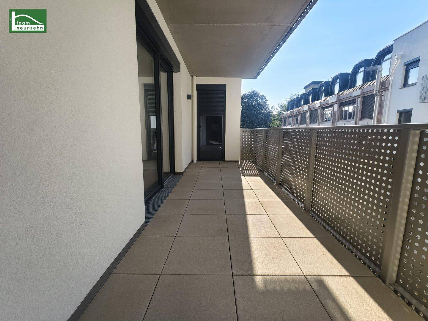 Langer, gefliester Balkon mit moderner Lochblech-Brüstung und Blick auf die Umgebung.