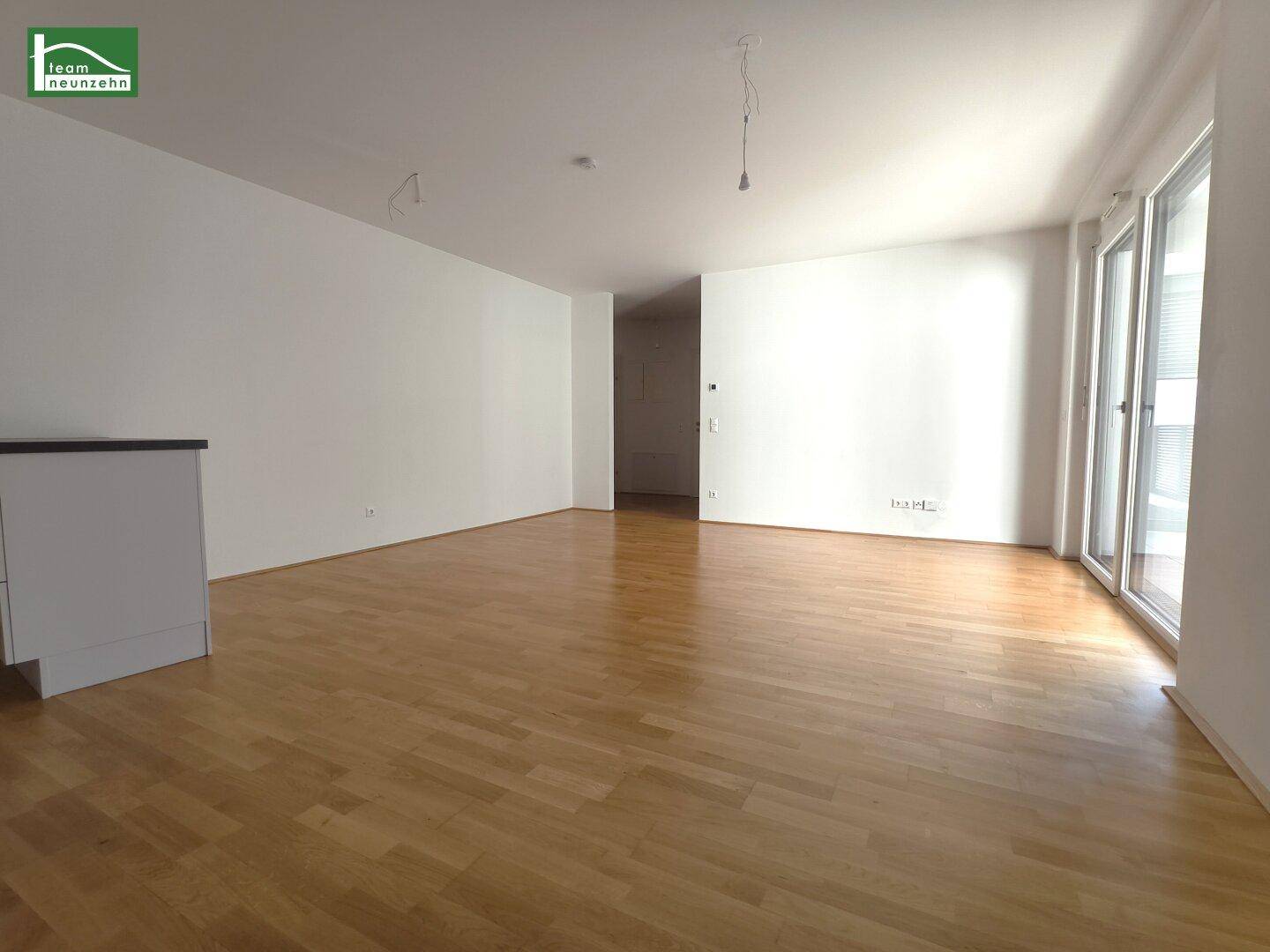 Geräumiger Wohnbereich mit hellem Parkettboden und Zugang zu einem sonnigen Außenbereich.