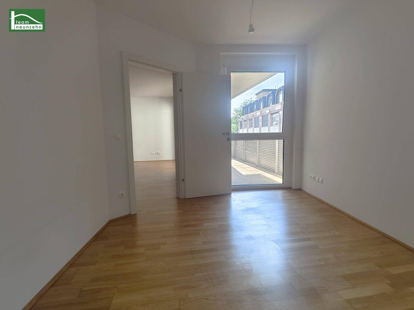 Lichtdurchflutetes Zimmer mit Parkettboden und Tür zum Balkon, bietet eine angenehme Wohnatmosphäre.
