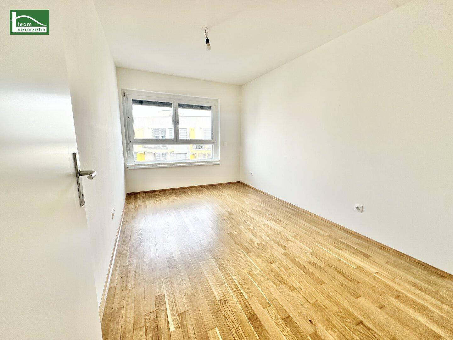 Leeres Schlafzimmer mit Parkettboden und einem Fenster, das viel Licht hereinlässt.