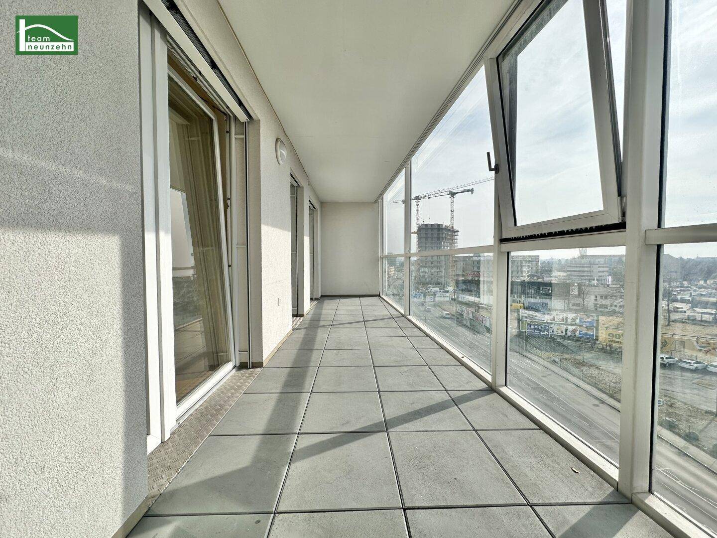 Lange Loggia mit Fliesenboden und Glasfront, die einen weiten Blick auf die Stadt bietet.
