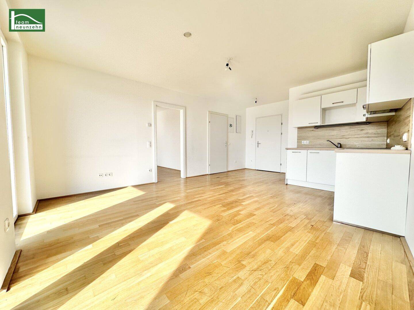 Heller offener Wohnbereich mit Parkettboden und integrierter Küchenzeile in einem modernen Apartment.