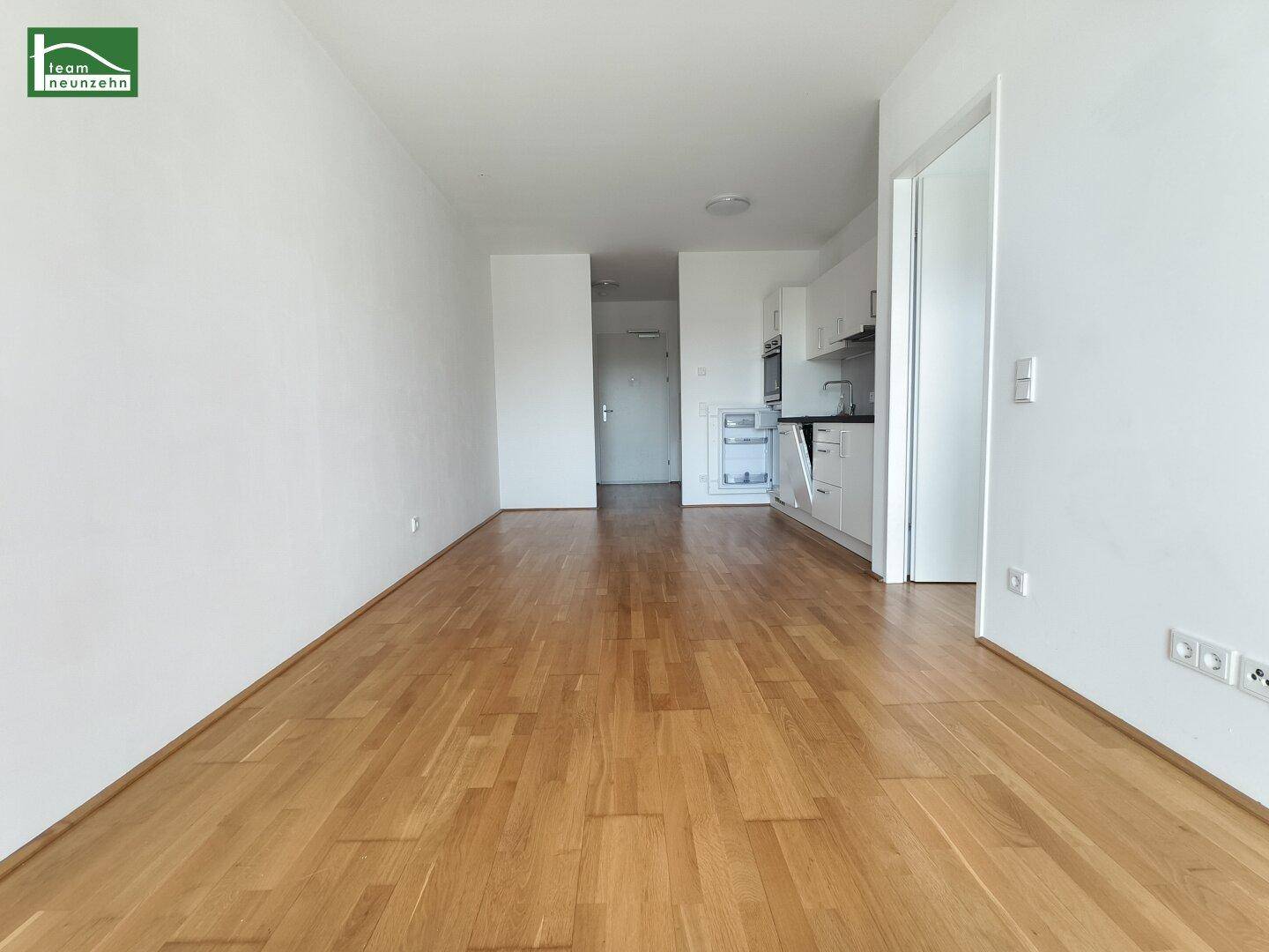 Offener Wohnbereich mit hellem Eichenparkett und integrierter Küchenzeile.