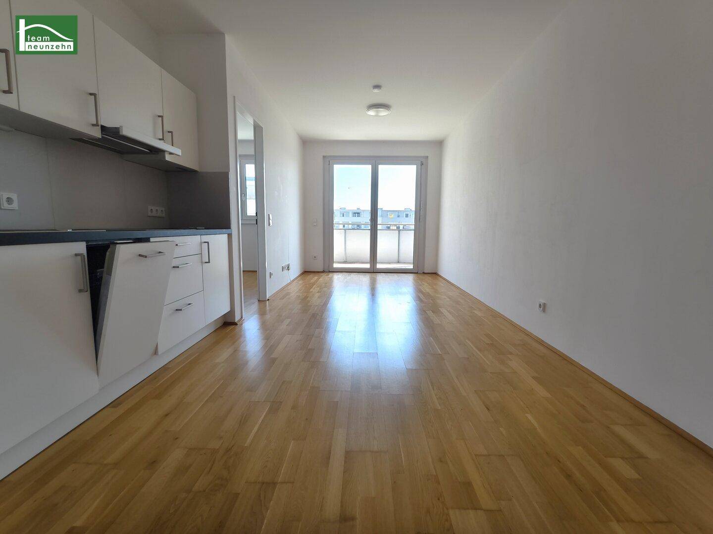 Heller offener Wohnbereich mit Eichenparkettboden und Zugang zu einem Balkon.