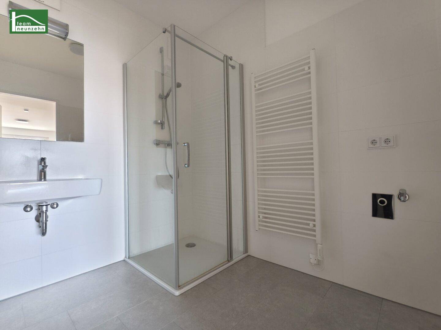 Modernes Badezimmer mit Duschkabine, Waschbecken und beheiztem Handtuchhalter.