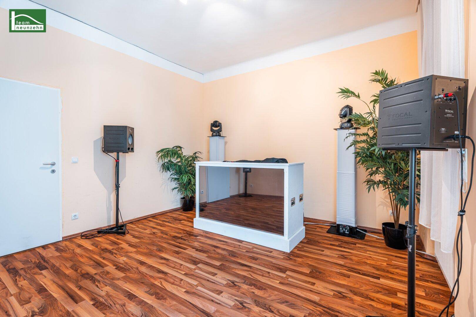 Heller Raum mit Laminatboden, DJ-Pult und Lautsprechern.
