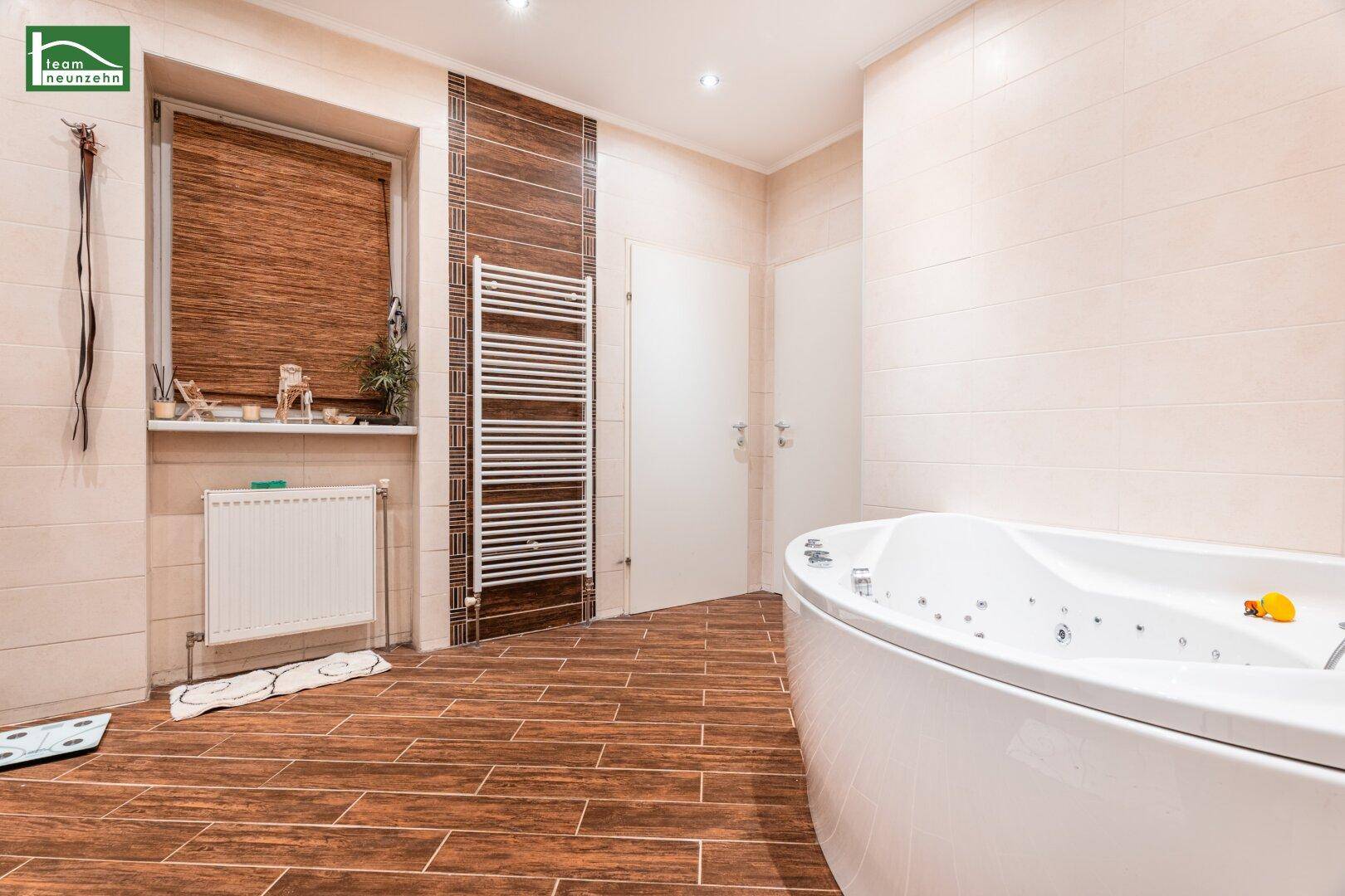 Helles Badezimmer mit Eckbadewanne, Fenster und beheiztem Handtuchhalter.