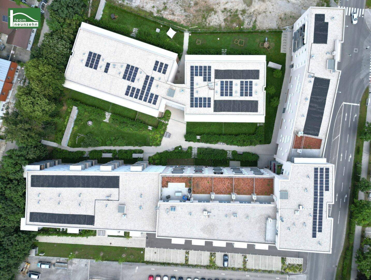 Vogelperspektive auf einen Wohnkomplex mit Flachdächern und Solaranlagen, umgeben von Grünflächen.