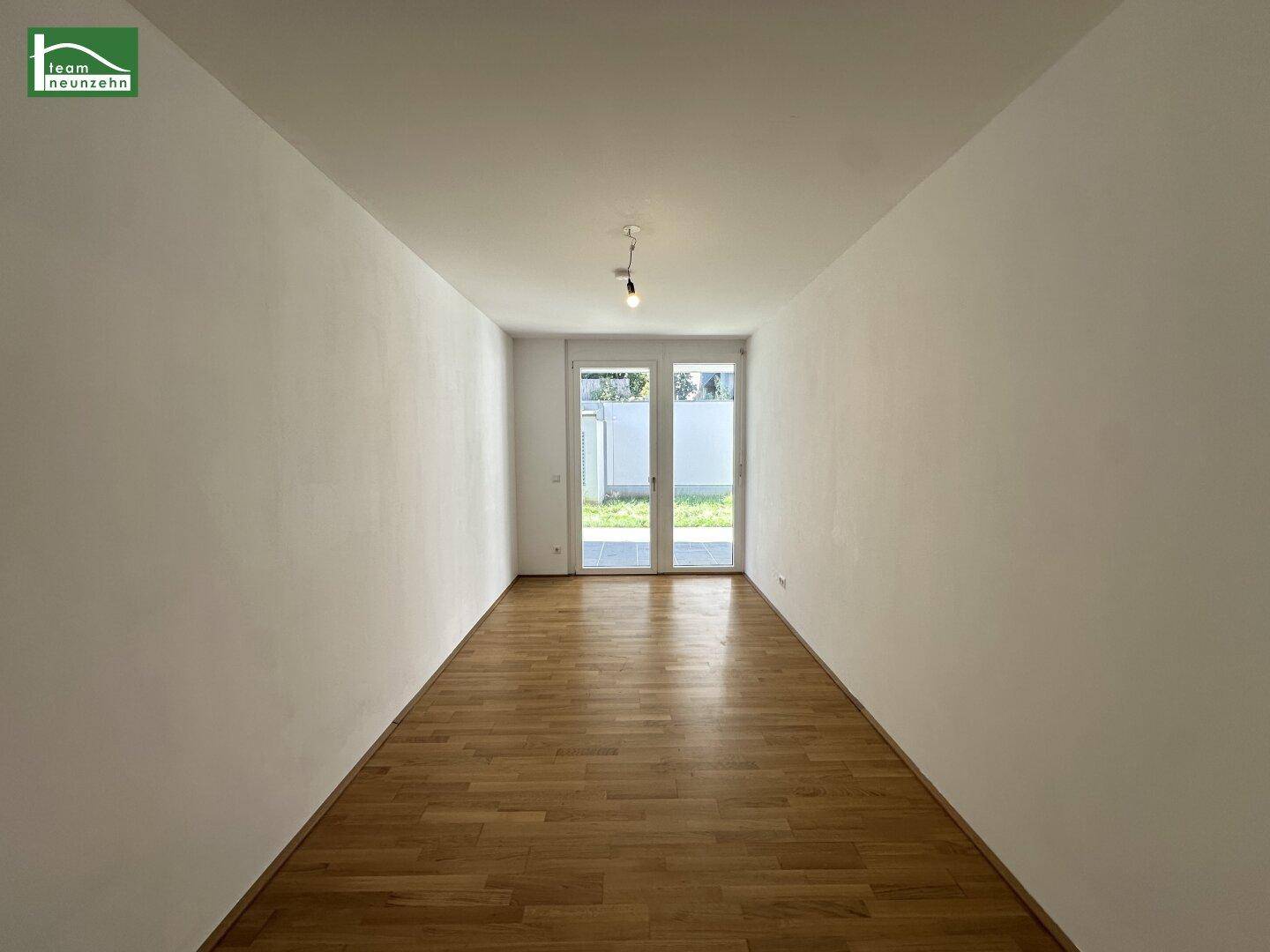 Leerer Raum mit Parkettboden und großen Fenstern, die viel Tageslicht hereinlassen.