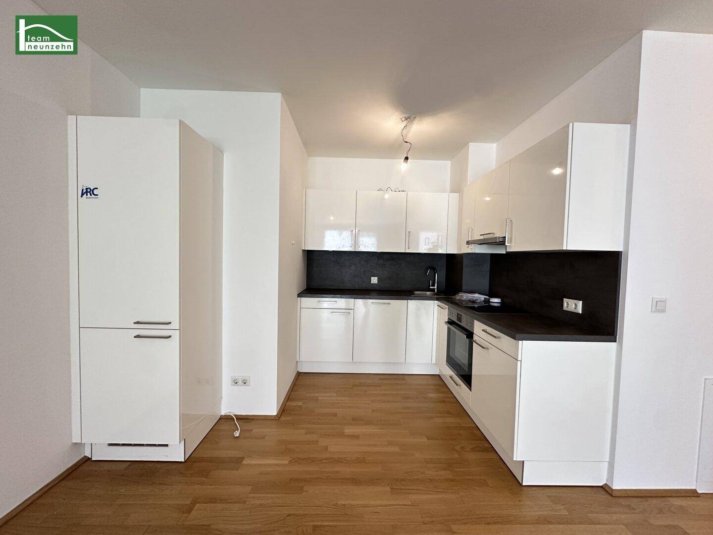 Moderne Einbauküche mit weißen Hochglanzfronten, dunkler Arbeitsplatte und integrierten Geräten.
