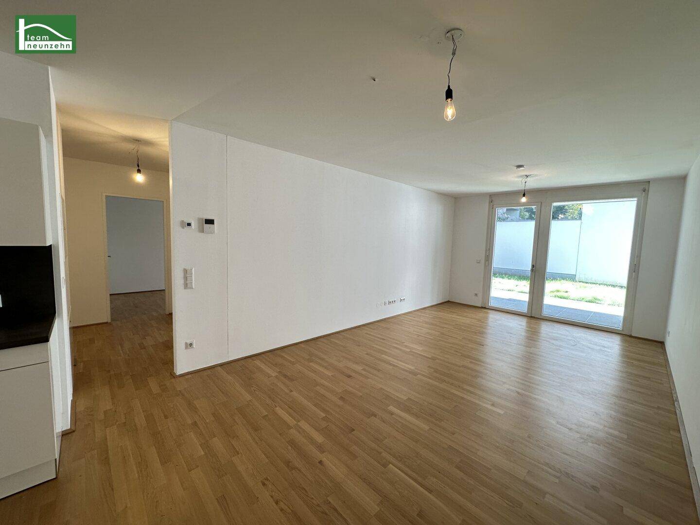 Geräumiger, leerer Wohn- und Essbereich mit Holzboden und großen Fenstern zum Außenbereich.