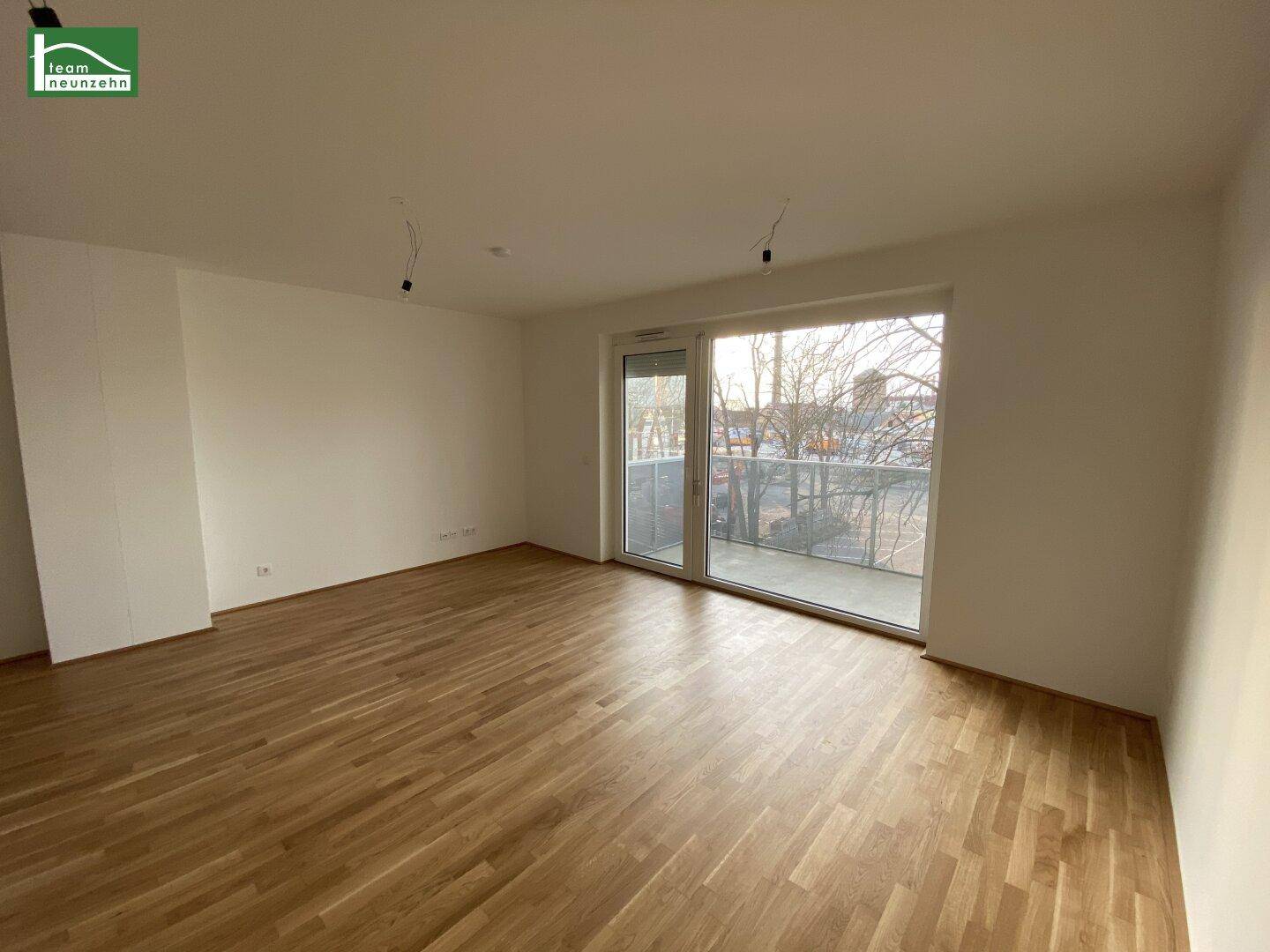 Geräumiger Wohnbereich mit hellem Parkettboden und breiter Fensterfront, die viel Tageslicht hereinlässt.