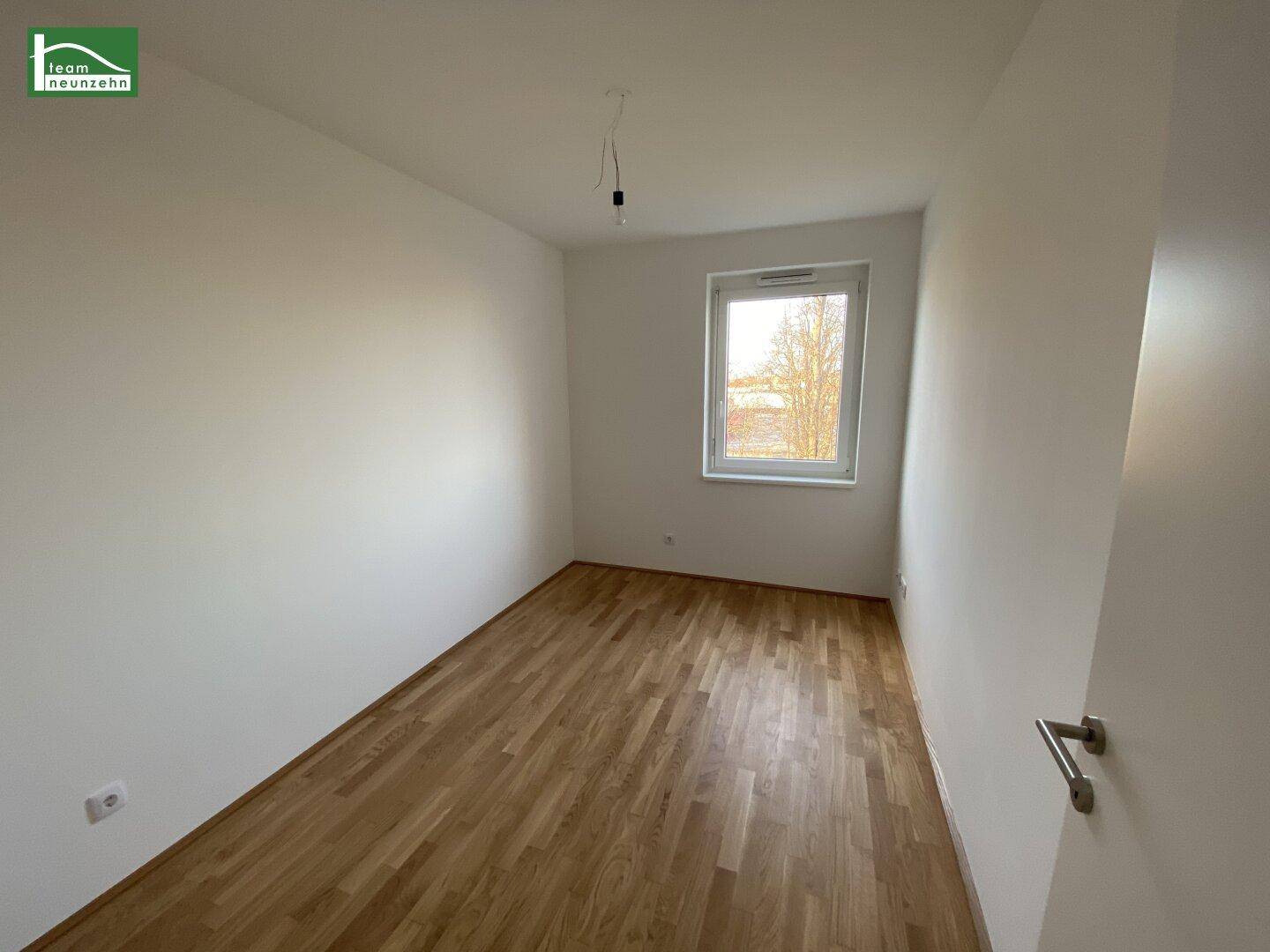 Helles Schlafzimmer mit Parkettboden und einem Fenster, das viel natürliches Licht spendet.