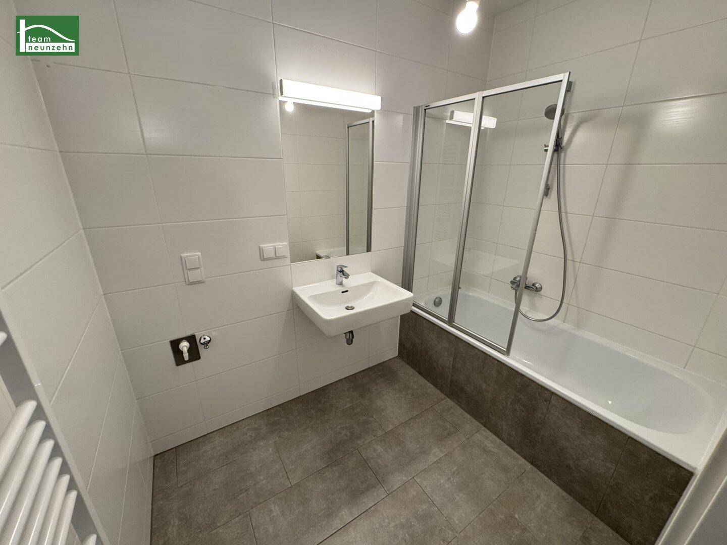 Modernes Badezimmer mit Badewanne, Duschwand, Einzelwaschbecken und beheiztem Handtuchhalter.