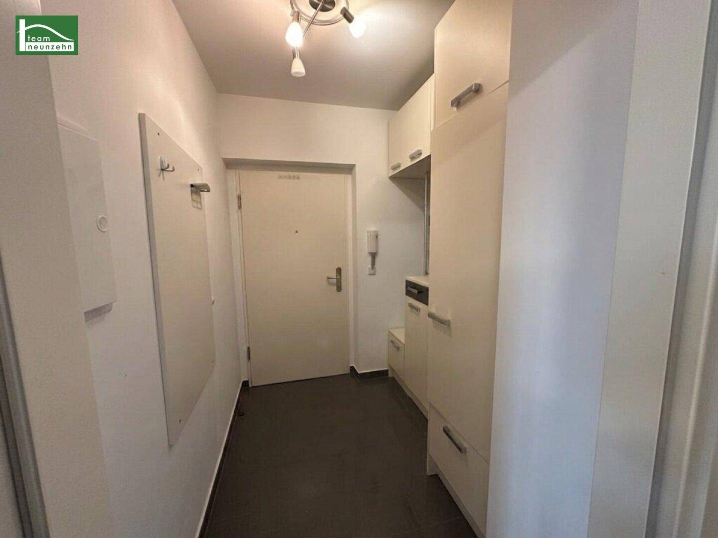 Heller Flur mit praktischen Einbauschränken und dunklem Fliesenboden im Eingangsbereich.