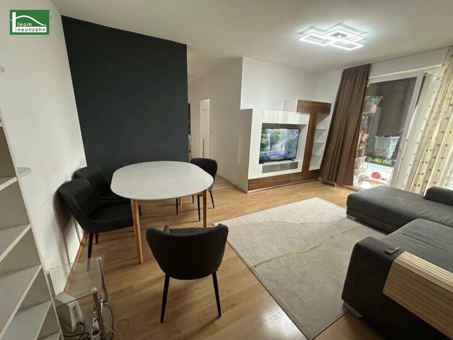 Moderner Wohn-Essbereich mit Holzboden, dunkler Akzentwand und Zugang zu einem Außenbereich.