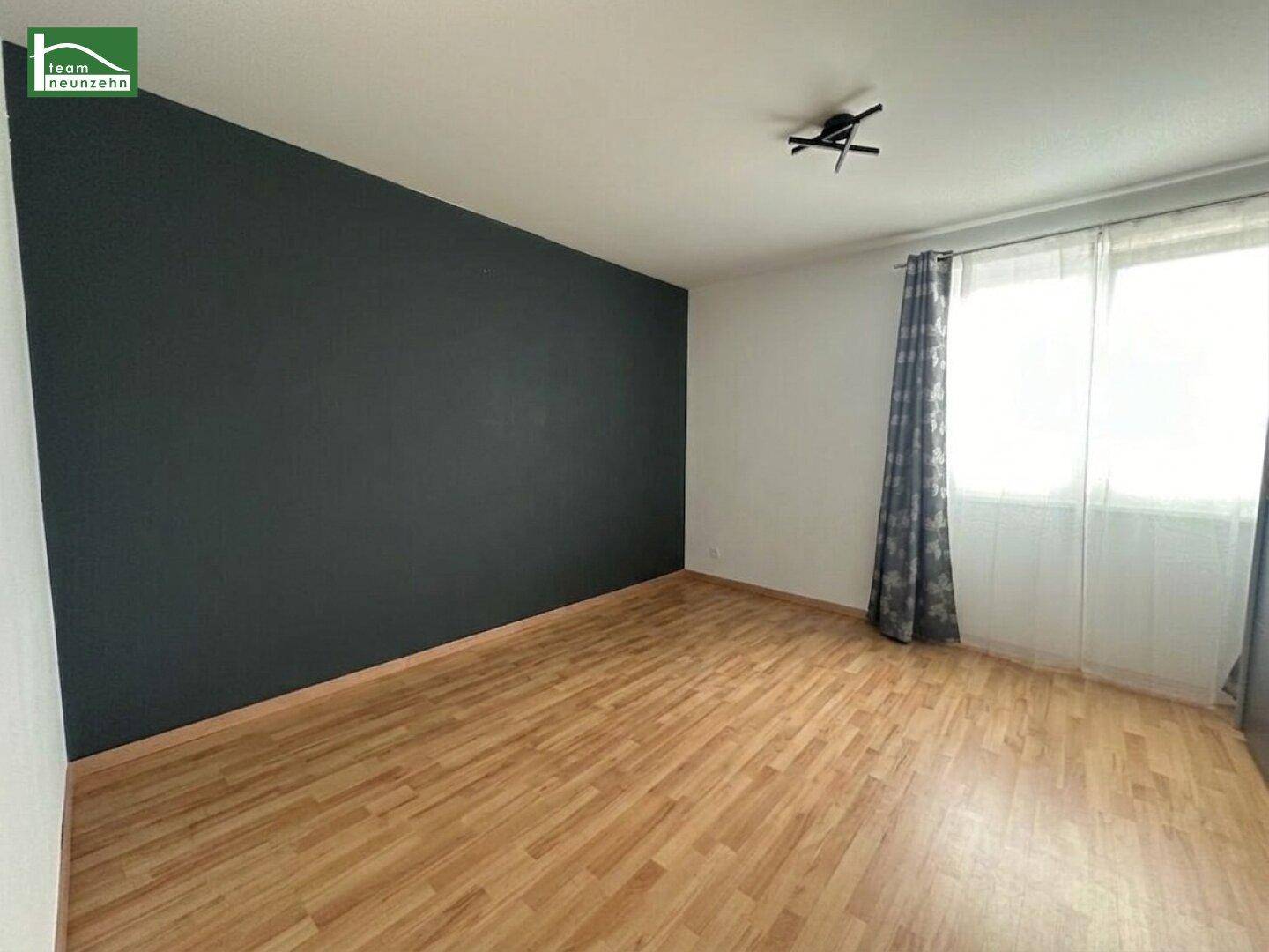 Geräumiges Zimmer mit Laminatboden, dunkler Akzentwand und großen Fenstern für viel Licht.