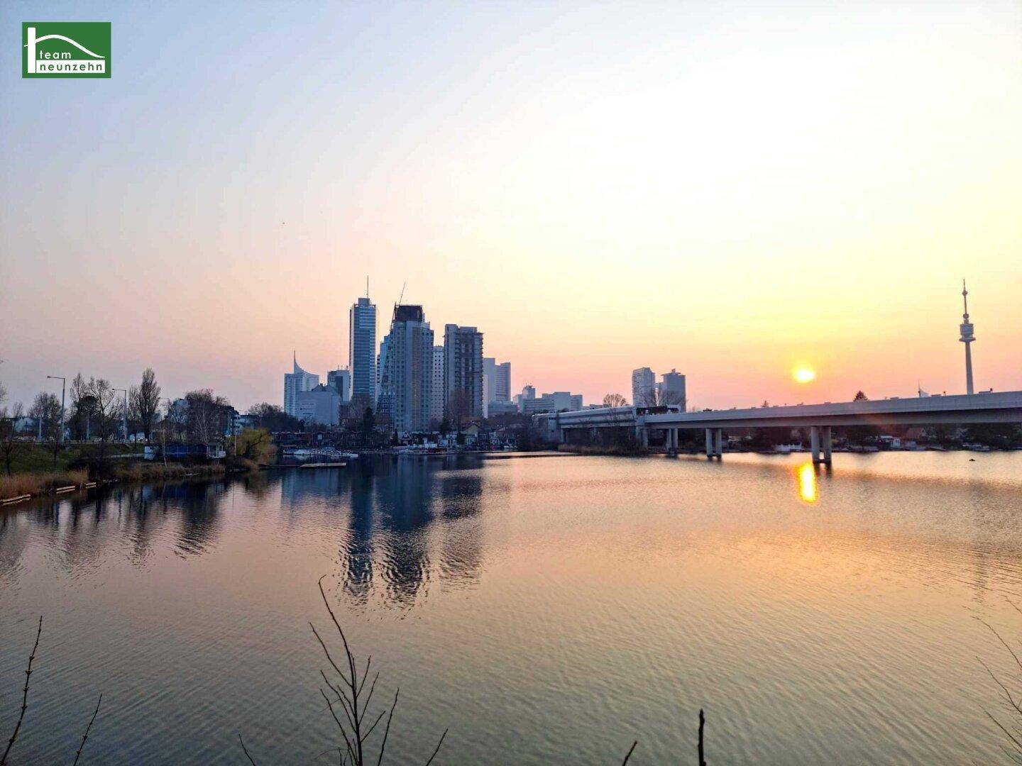 Panoramablick auf die Stadt bei Sonnenuntergang mit Fluss, modernen Gebäuden und Brücke.