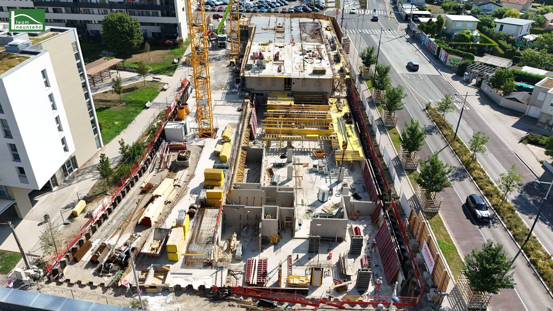 Detailansicht einer Baustelle von oben, mit Baugeräten und angrenzenden Straßen und Gebäuden.