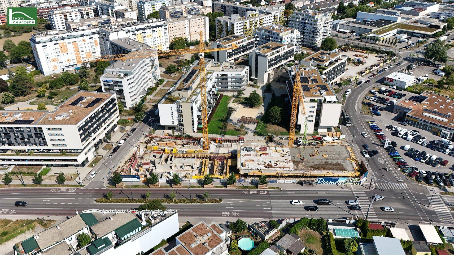 Panoramische Luftaufnahme der Baustelle in einem städtischen Umfeld mit zahlreichen Wohngebäuden und Grünflächen.