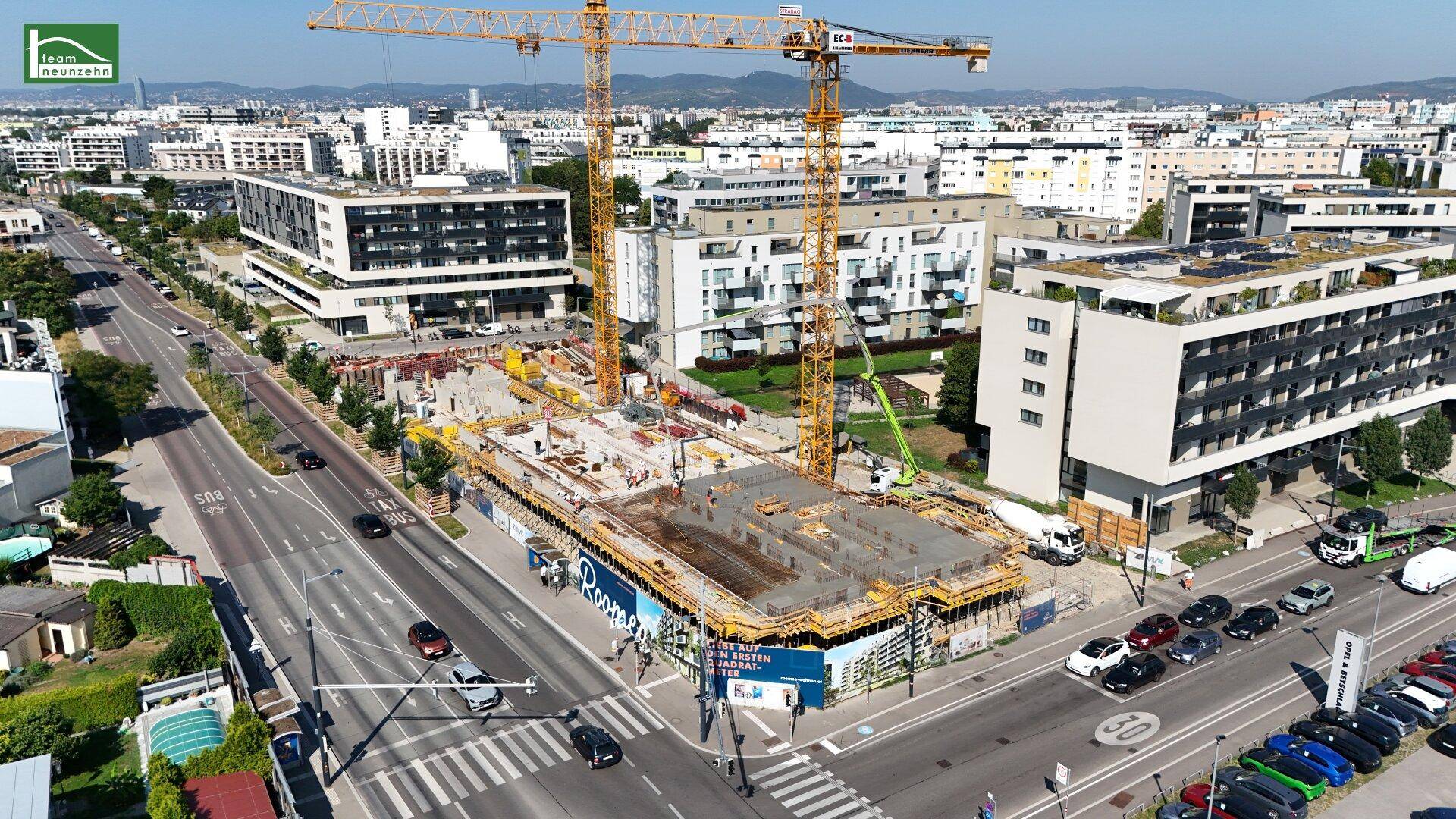 Nahaufnahme der Baustelle mit fortgeschrittenem Fundamentbau, Kränen und angrenzenden modernen Wohngebäuden.