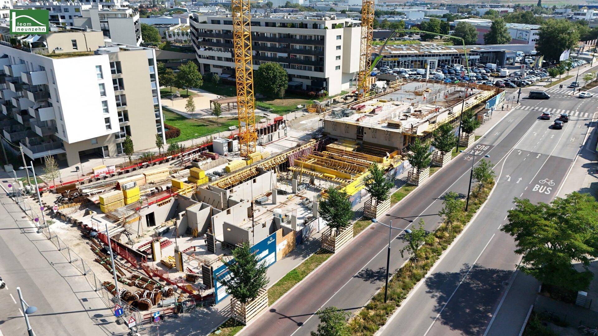 Luftbild der Baustelle mit Kränen, umgeben von modernen Wohngebäuden und einer belebten Hauptstraße.
