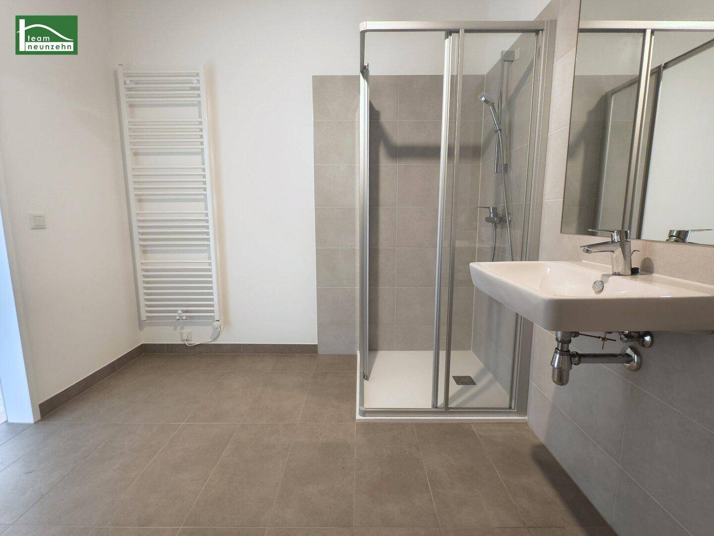 Modernes Badezimmer mit grauen Fliesen, Duschkabine, Waschbecken und beheiztem Handtuchhalter.